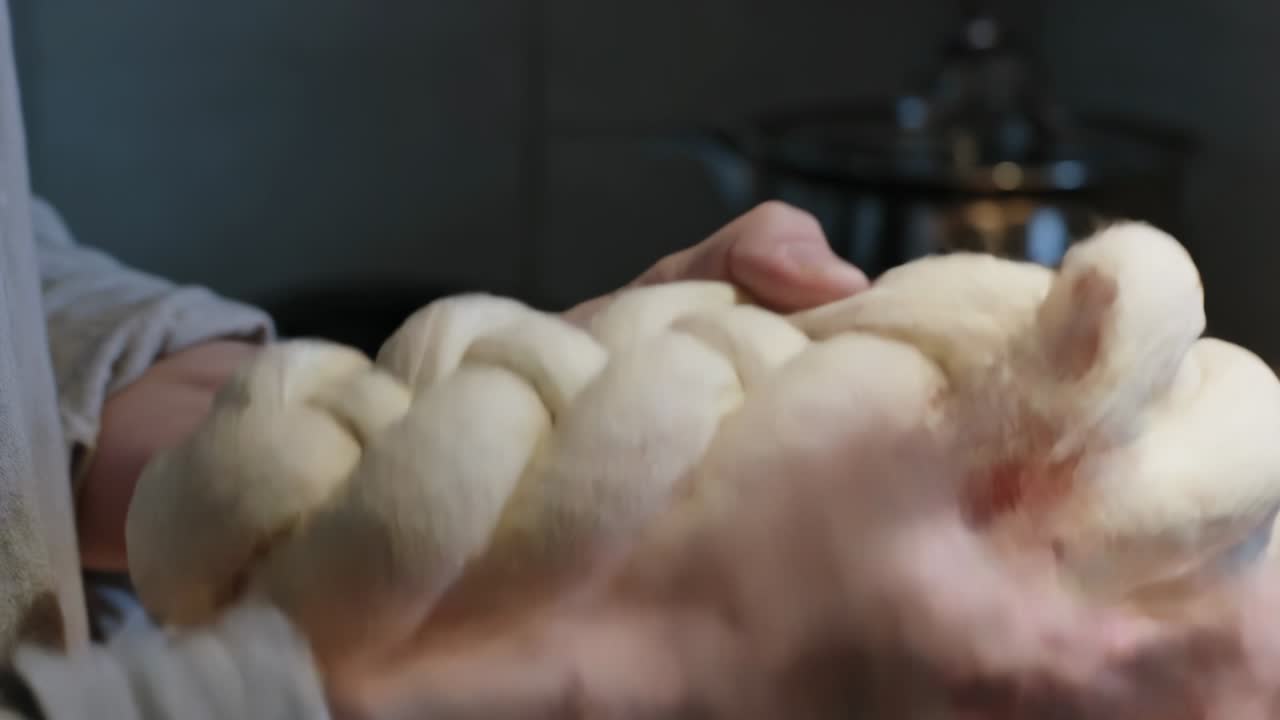 Panettiere in camice afferra una pagnotta, sistema e leviga l'impasto intrecciato in cucina, preparandolo per la cottura.