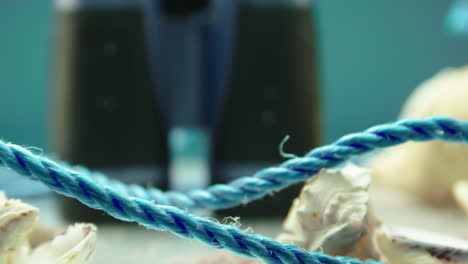 video de primer plano de una cuerda azul y conchas marinas, rodeadas de arena de playa, en una pantalla giratoria con binoculares en el fondo