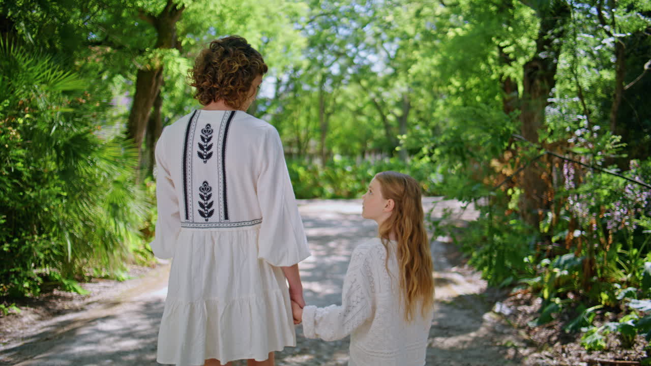 Back view family walking at sunny park. Young mother strolling cute daughter
