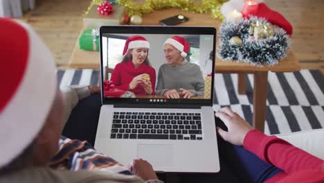 African-american-mother-and-daughter-using-laptop-for-christmas-video-call-with-family-on-screen