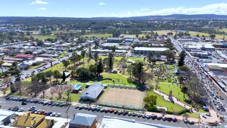 drone footage captures a vibrant outdoor festival along a main road in a small australian town, with crowds, green parkland, and clear daylight