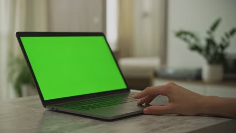la mano de una mujer caucásica deslizando en un touchpad de portátil con una pantalla verde de tecla de croma en él