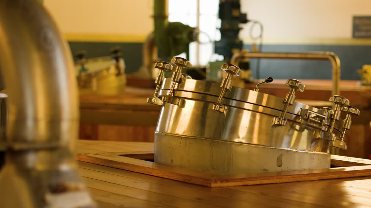 Slow pan across wooden washbacks and metal hatches in warmly lit distillery fermentation room