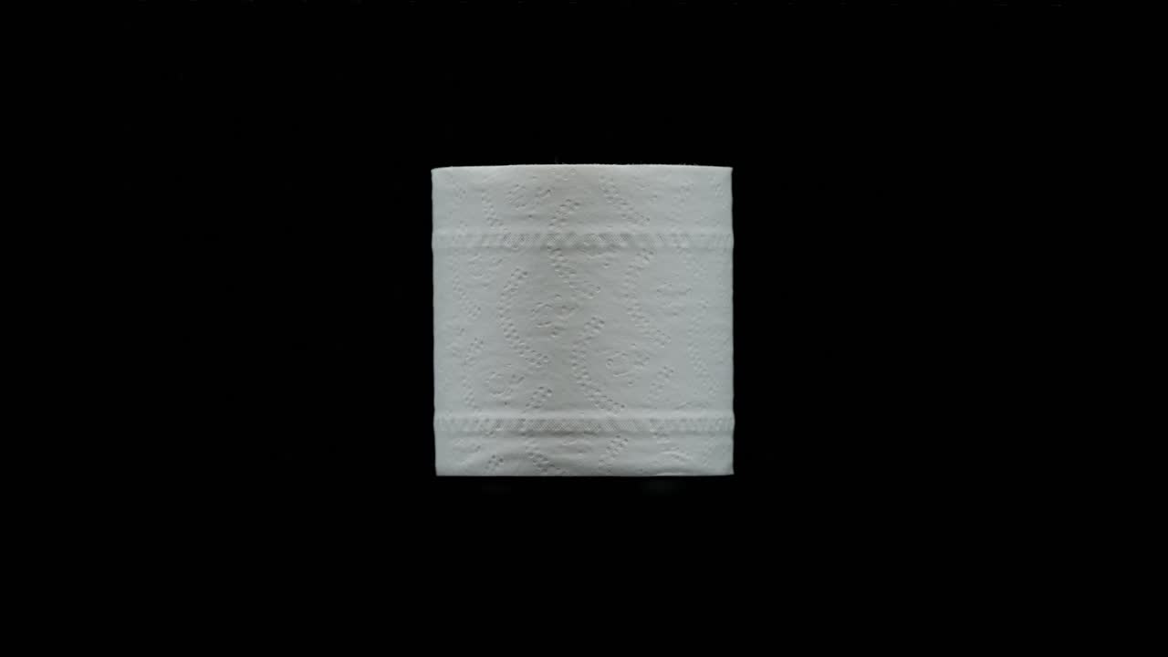 Studio shot of a single toilet paper roll slowly rotating on black background with clean minimal lighting