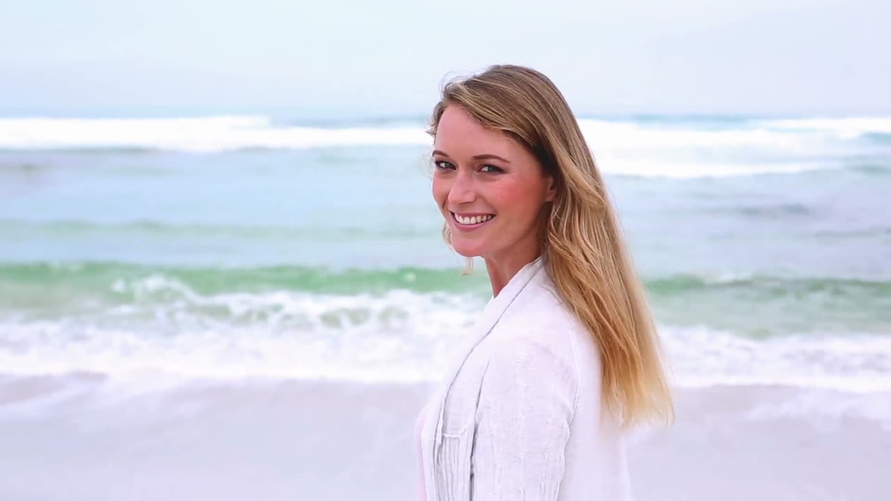 해변에서 행복한 금발이 돌아서서 카메라에 미소를 짓고 있습니다.