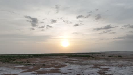 Aerial-drone-tilt-up-shot-over-largest-natural-salt-resource-from-a-dried-lake-in-Nagarparkar,-Sindh,-Pakistan-with-sun-rising-in-the-background