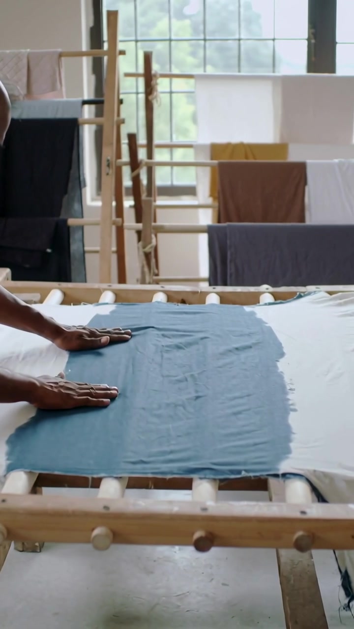 Vertical video: Coming worker in shirt pressing evening blue dye on frame near window with racks
