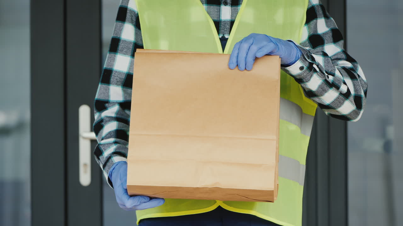 장갑을 낀 택배원이 음식 한 봉지를 들고 있다