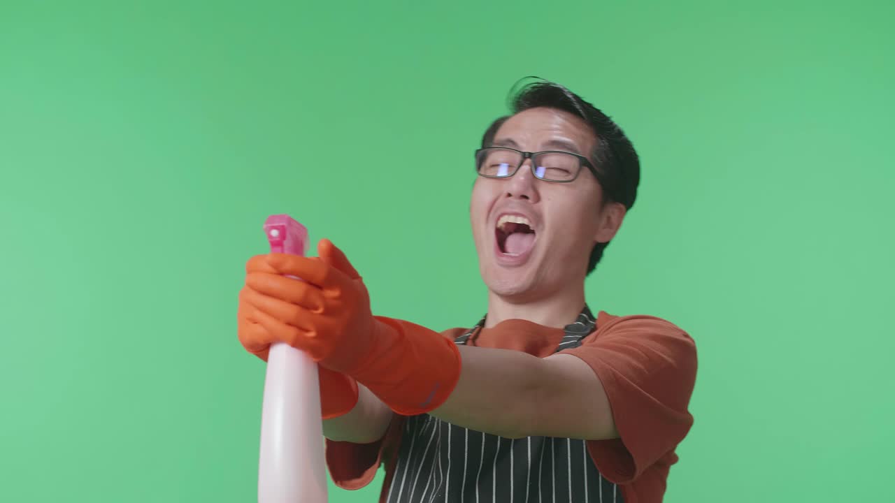 녹색 스크린 스튜디오에 서 있는 동안 스프레이를 사용하여 전신을 가진 재미있는 아시아 남성 집주인의 클로즈업