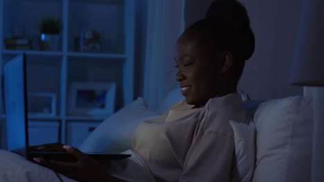 African-Woman-with-Laptop-in-Bed-at-Home-at-Night.technology,-internet,-communication-and-people-concept-young-african-american-woman-with-laptop-computer-lying-in-bed-at-home-at-night