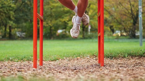 Beine-Eines-Athletischen-Sportlers,-Der-Klimmzüge-In-Der-Roten-Sportanlage-Im-Park-Macht