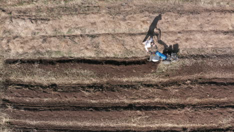 aerial - man working a field with a rototiller, agriculture in sweden, wide shot