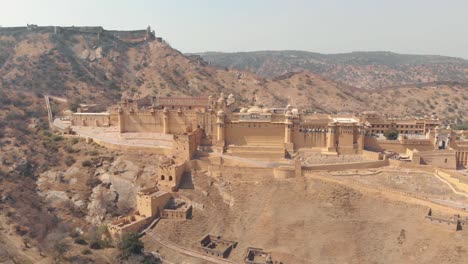 amber fort standing on foot of barren mountain surrounded by hills and ridges in jaipur, rajasthan, india - aerial ascending tilt-down wide shot