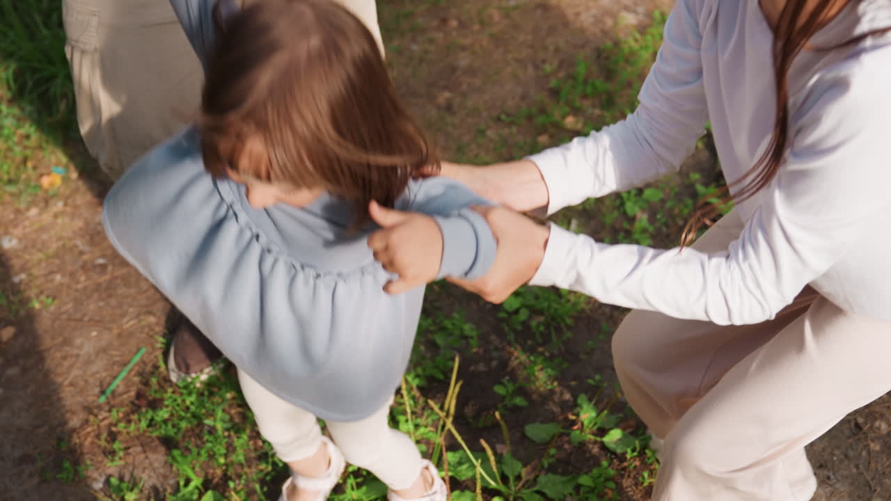 Aerial view of youngsters strolling together on forest path holding hands, joyfully lifting youngest sibling between them, surrounded by green trees, creating warm outdoor family bonding moment