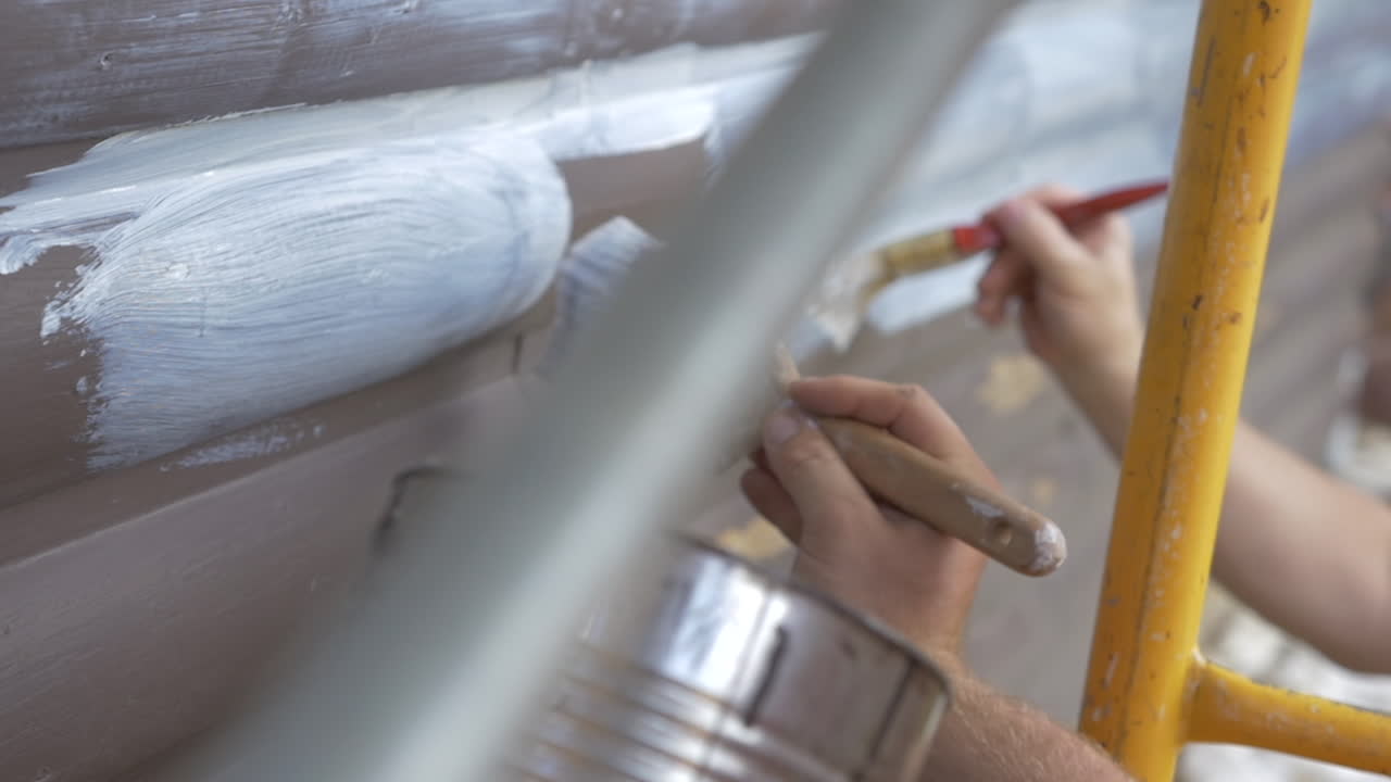 갈색 통나무집에 프라이머를 바르고 있는 두 사람이 클로즈업