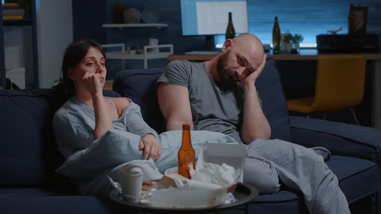 Depressed, frustrated young couple sitting in couch suffering from insomnia