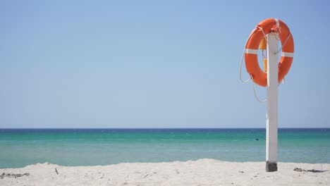 an orange lifebuoy hangs from a pole on a sandy beach against a blue sky and azure sea