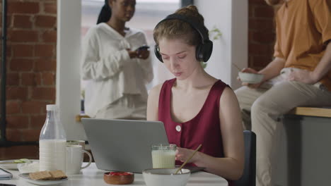 girl with headphones working on laptop computer during breakfast in a shared flat