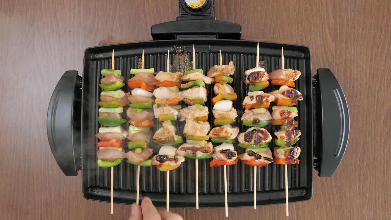Uomo che cucina spiedini di pollo e verdure su una griglia elettrica compatta e calda