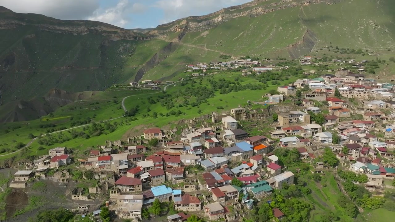 Riprese drone del villaggio di Chokh con case tradizionali su un ripido pendio montano, valli verdi e creste spettacolari sotto un cielo nuvoloso nel Dagestan, Russia, Caucaso.