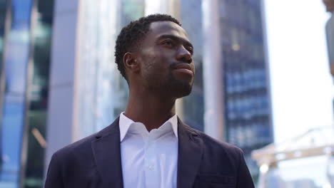 Portrait-Of-Confident-Young-Businessman-Wearing-Suit-Standing-Outside-Looking-Up-At-Offices-In-The-Financial-District-Of-The-City-Of-London-UK-1