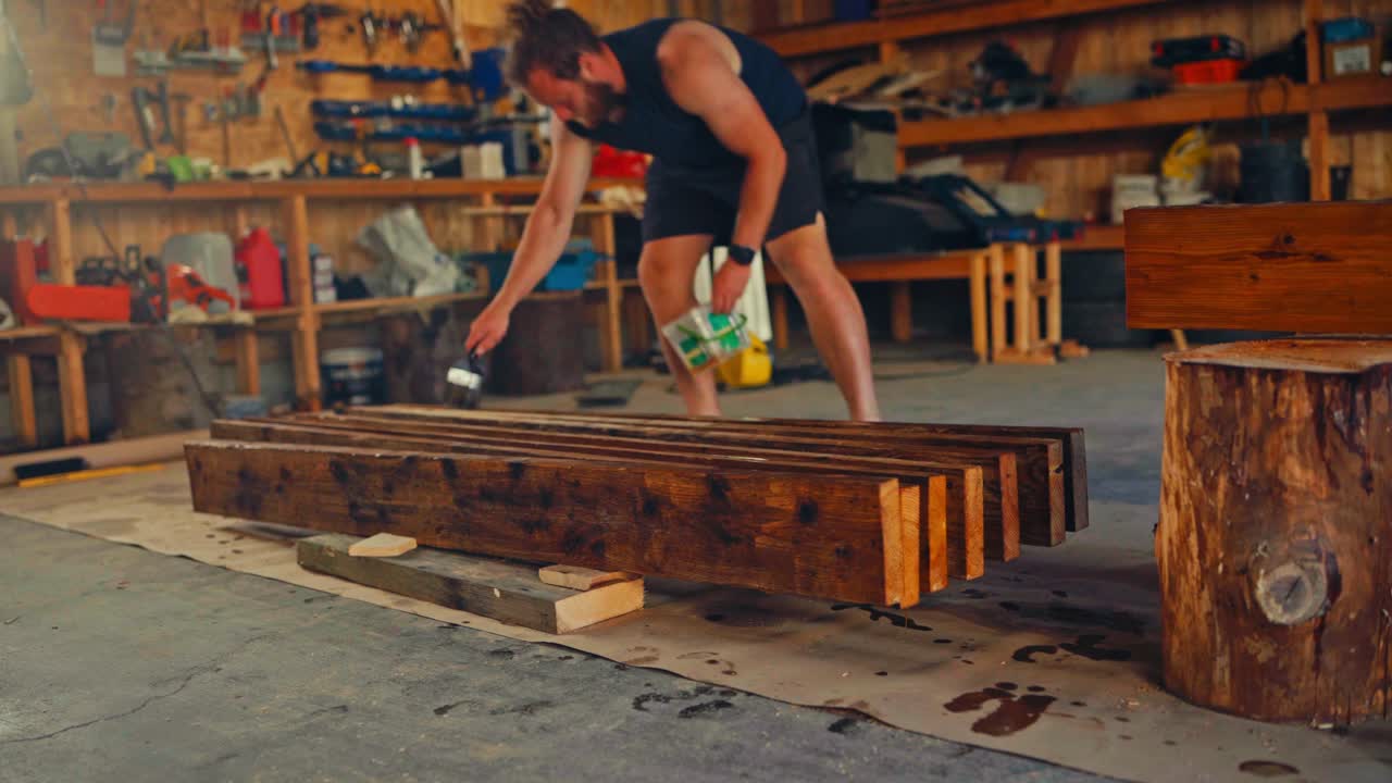 A Man is Applying a Coat of Finish to Wooden Planks in a Workshop - Static Shot