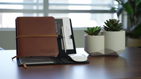 an organized workspace featuring a notebook, pen, and succulent plants on a modern desk with natural light streaming through large windows