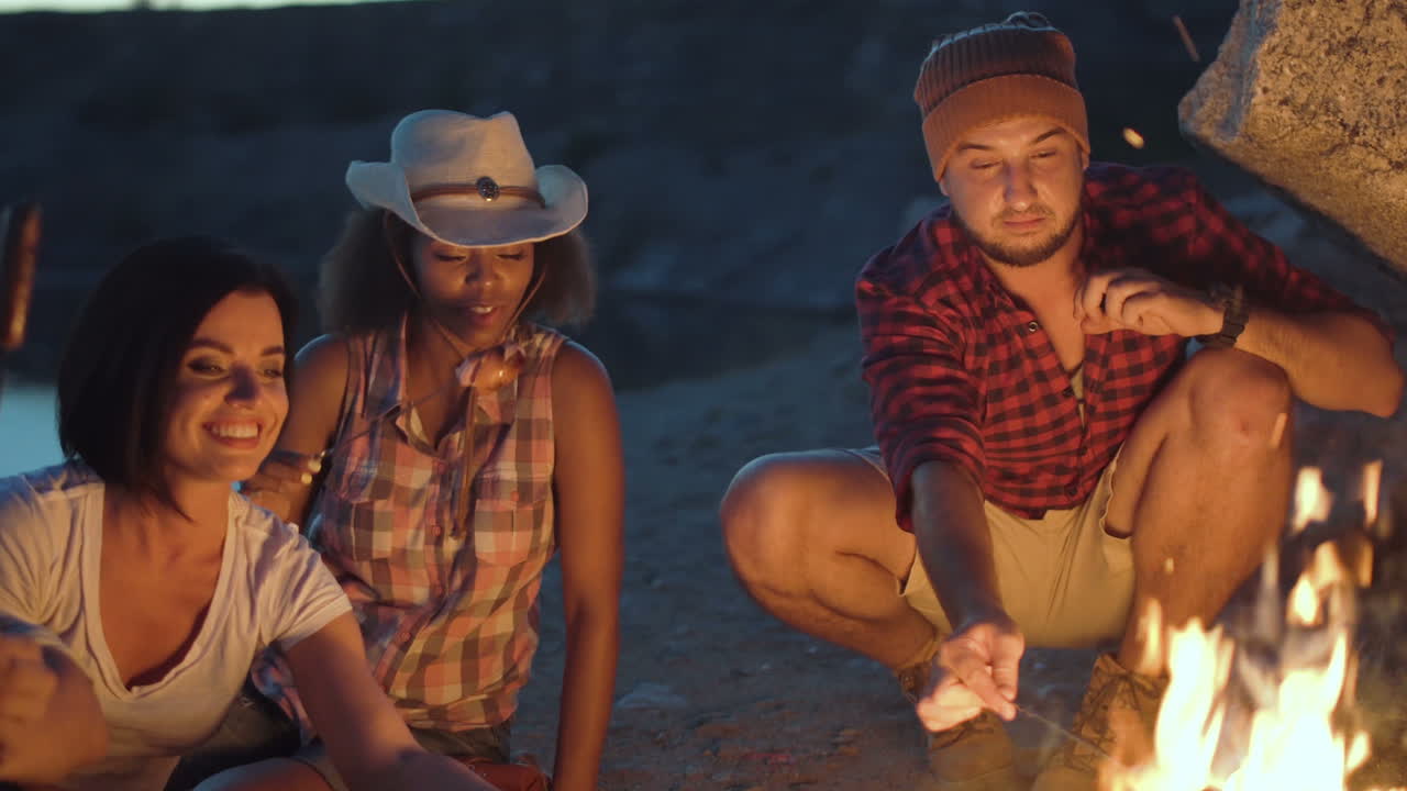 Friends roasting sausages on a campfire at night