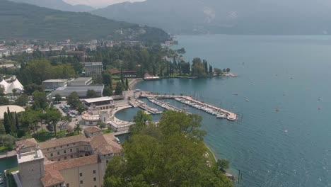 beautiful drone shot of the harbor in riva del garda with an old castle in the foreground and the lake garda and italian alps in the background