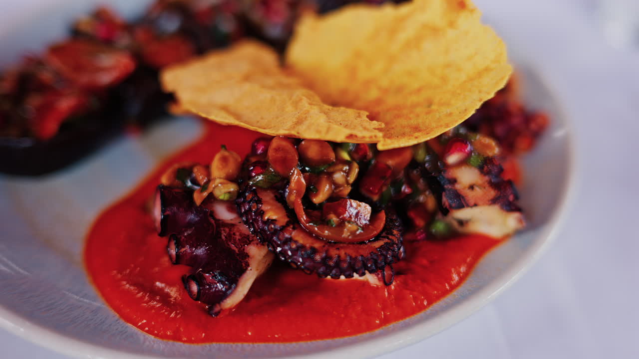 Close up of grilled octopus on a plate, garnished with a rich red sauce