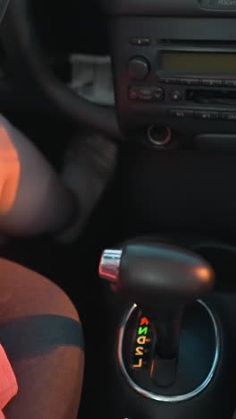 mujer en vestido rosa sentada en su coche alcanza la taza de café cerca del cambio de marchas y toma un sorbo, el interior del coche está ligeramente borroso con reflejos suaves de luces de paso que la iluminan