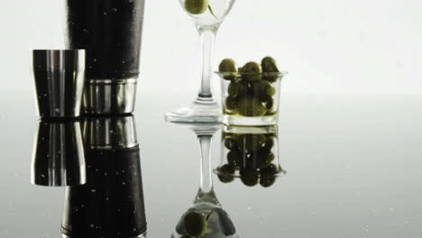 white particles floating over bartender equipment and olives in cocktail glass on grey background