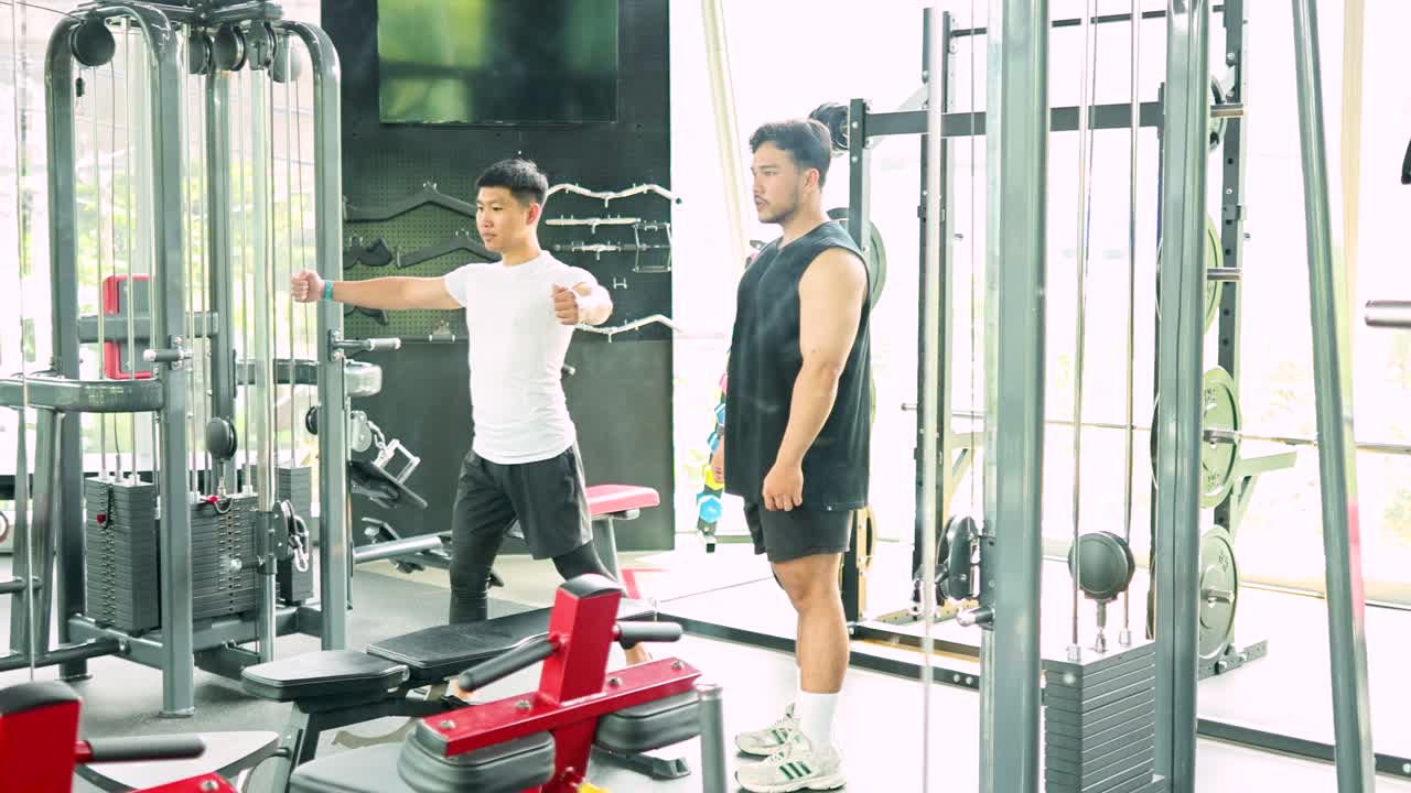 Two men exercise in a gym, using weight machines under bright lighting, showcasing teamwork and fitness