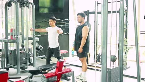 two men exercise in a gym, using weight machines under bright lighting, showcasing teamwork and fitness
