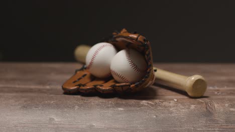 studio baseball shot with ball in catchers mitt and person picking up wooden bat from wooden background