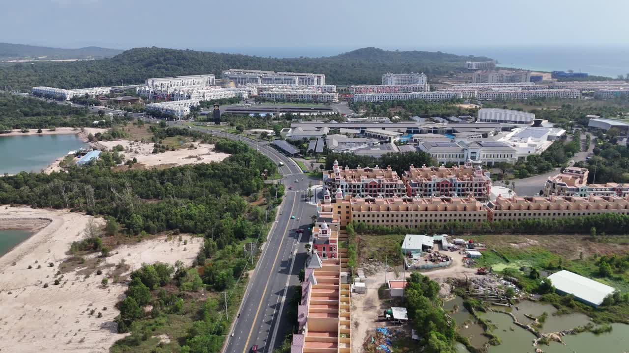 Aerial video reveals a newly built town showcasing a distinct architectural style with colorful buildings tightly lining developed with wide roads and some surrounding green spaces. a range of hills