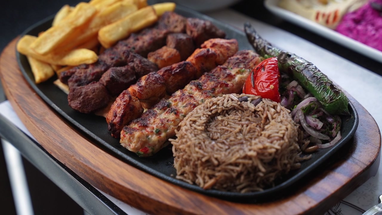 Primo piano di un piatto tradizionale di grigliata mista con spiedini di carne, shish di pollo, riso e patatine fritte su un tavolo di ristorante. Un vivace piatto di antipasti mediorientali con una morbida illuminazione interna.