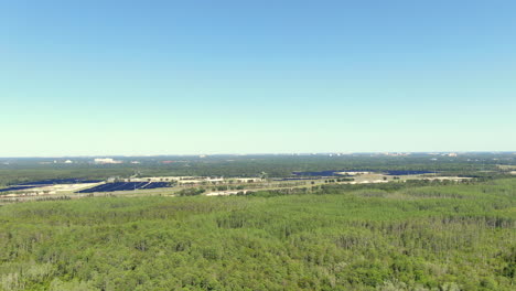 Panning-across,-thick,-lush,-green-woods-with-a-solar-farm-in-the-distance