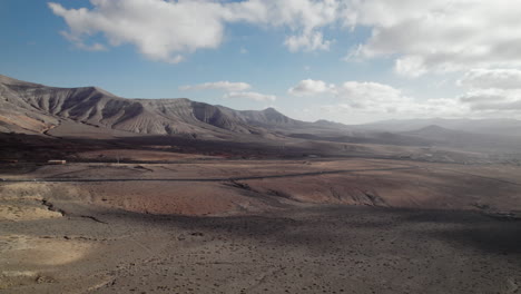 aerial shot of desert valley with mountain range on an island with desolate landscape and partly cloudy sky