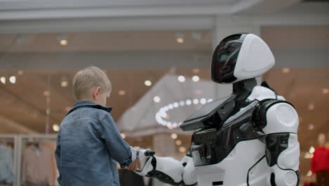 the boy stretches out his hand to the robot for a handshake