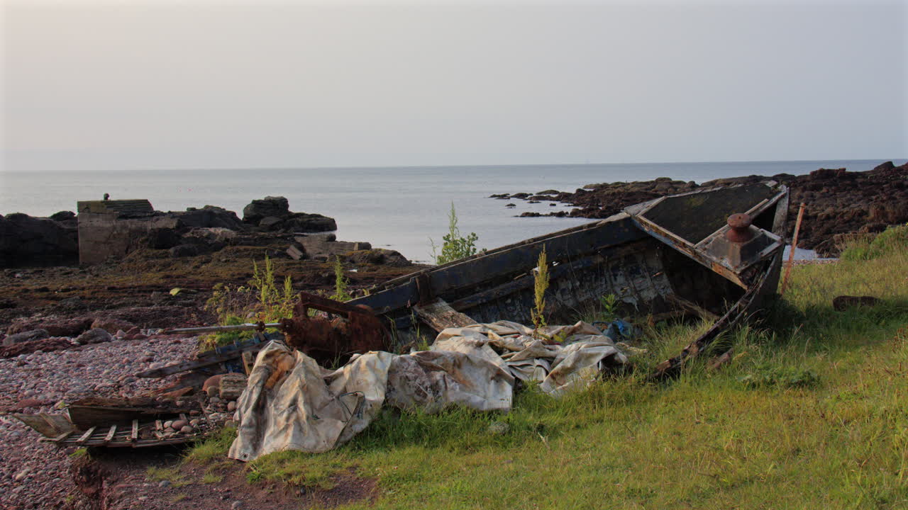 Wide shot of an abandoned derelict broken boat at the old harbour at low tide at Auchmithie