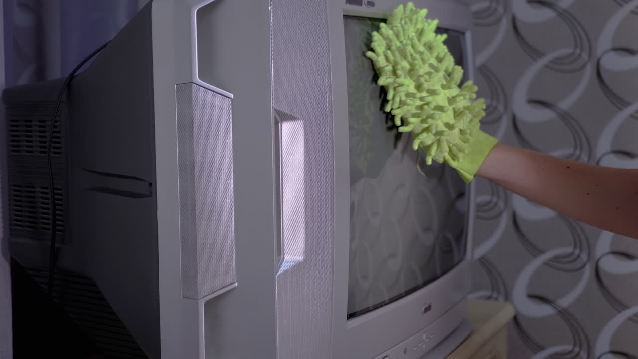 mano femenina en guantes naranjas limpia la pantalla de la vieja tv con un trapo de microfibra verde