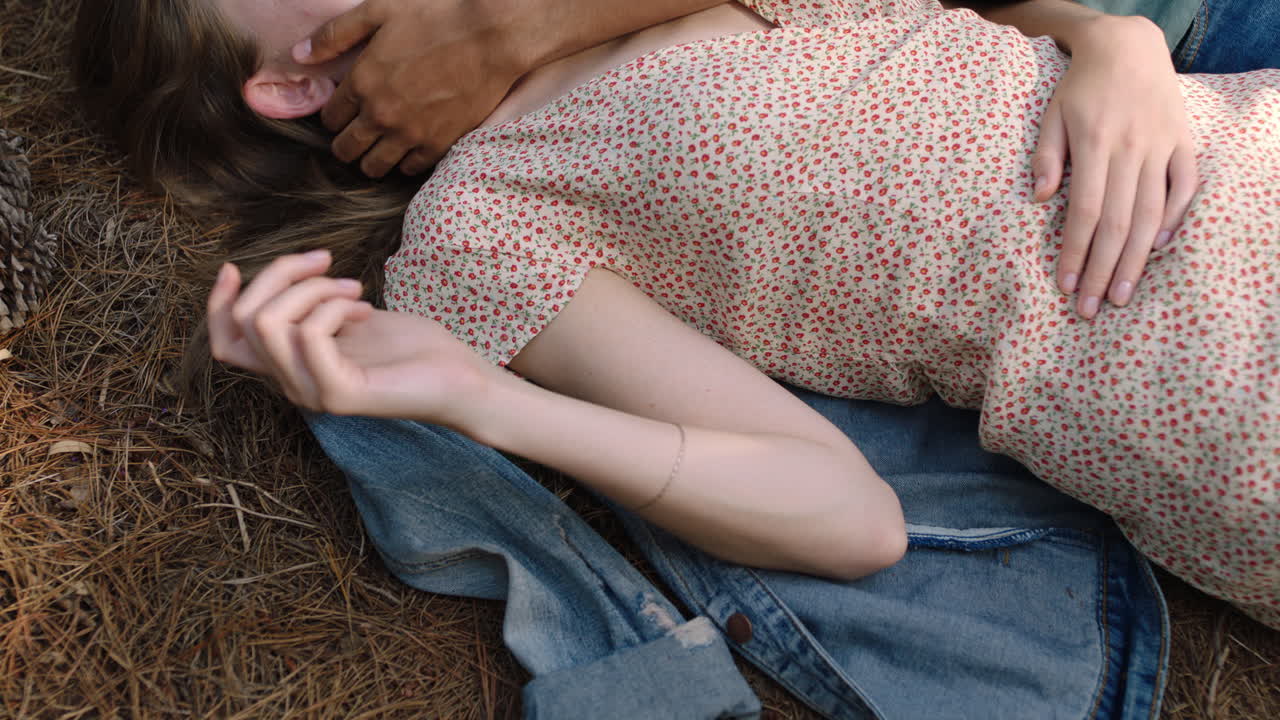 젊은 남자가 여자 얼굴을 손으로 만지며 부드럽게 만지며 애정을 나타 ⁇ 니다. 십대 부부는 숲에서 땅에 누워 있습니다.