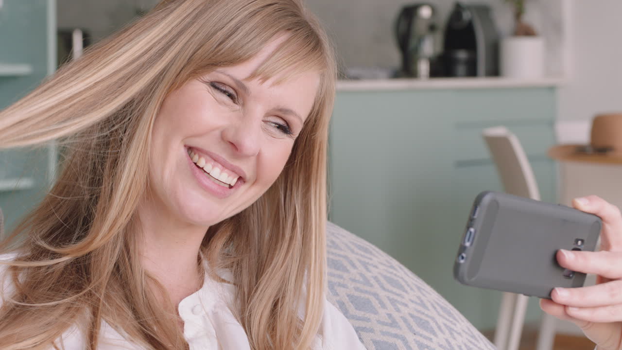 hermosa mujer rubia teniendo video chat usando un teléfono inteligente en casa mostrando su peinado hablando con un amigo compartiendo estilo de vida disfrutando de la comunicación en línea