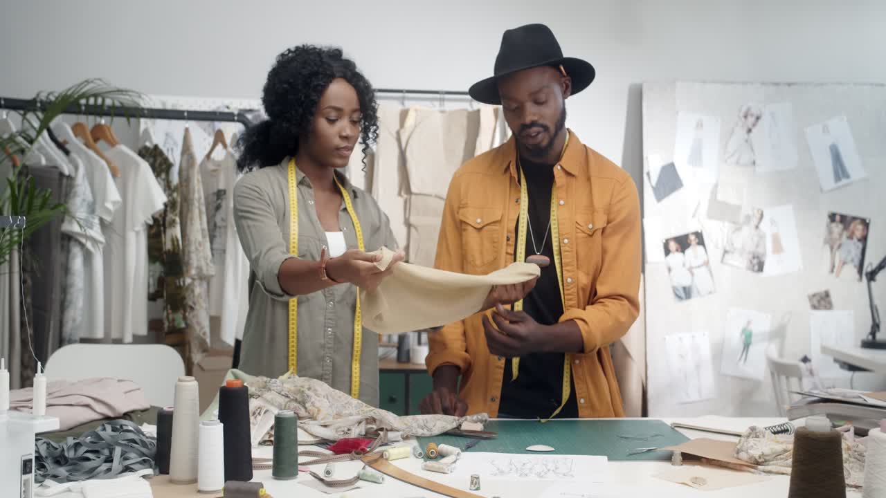 joven diseñadora mostrando una pieza de tela a su colega diseñador masculino