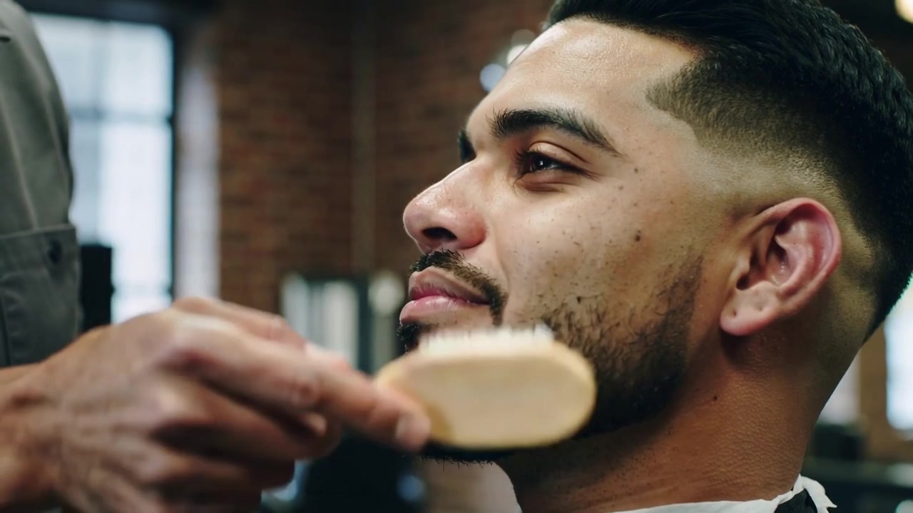 Mano del barbiere che spazzola la guancia del cliente con il mantello in barberia, rimuovendo i capelli con una spazzola di legno.