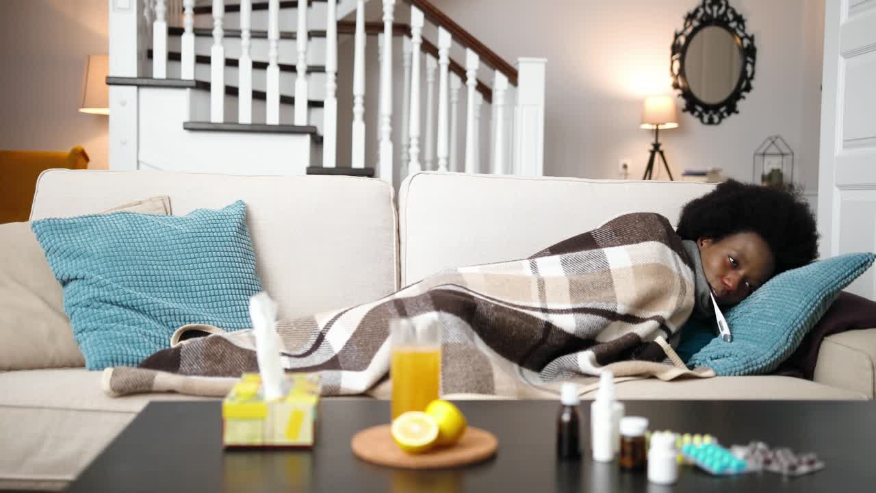 아프리카 계 미국인 여성, 매우 아프고 온도계를 입에 넣고 소파에 누워