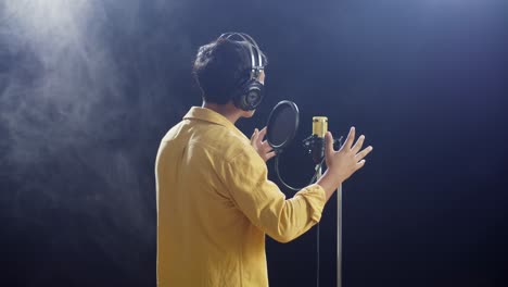 vista trasera de un niño con auriculares cantando en un micrófono condensador en el fondo negro de humo blanco