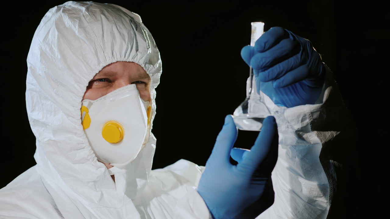 보호 복과 인공 호흡기를 입은 남자가 플라스크를 검사합니다 1