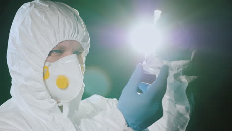 A-man-in-a-protective-suit-and-a-respirator-examines-a-flask-1